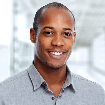 Young smiling African-american businessman over office background.